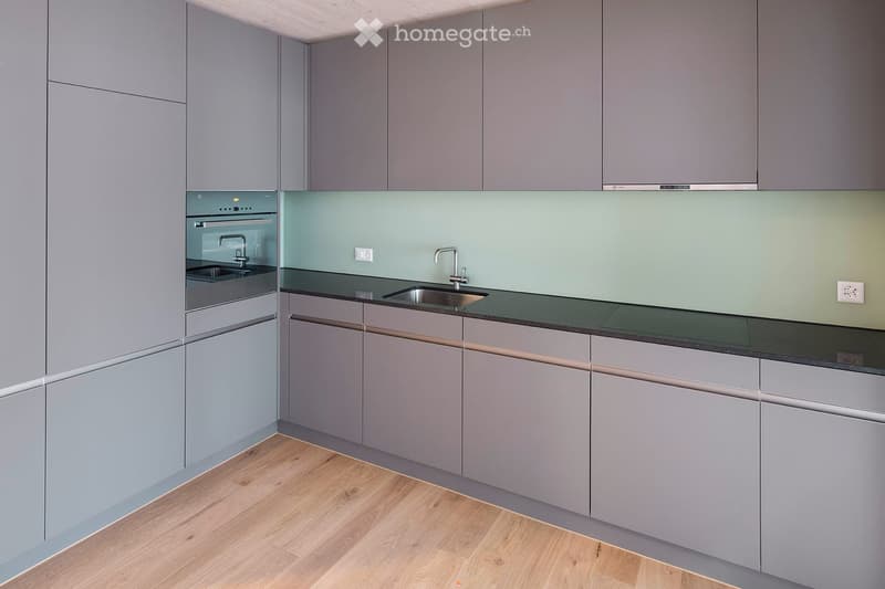 Modern kitchen with grey cabinets, black countertops, and a stainless steel sink and faucet.