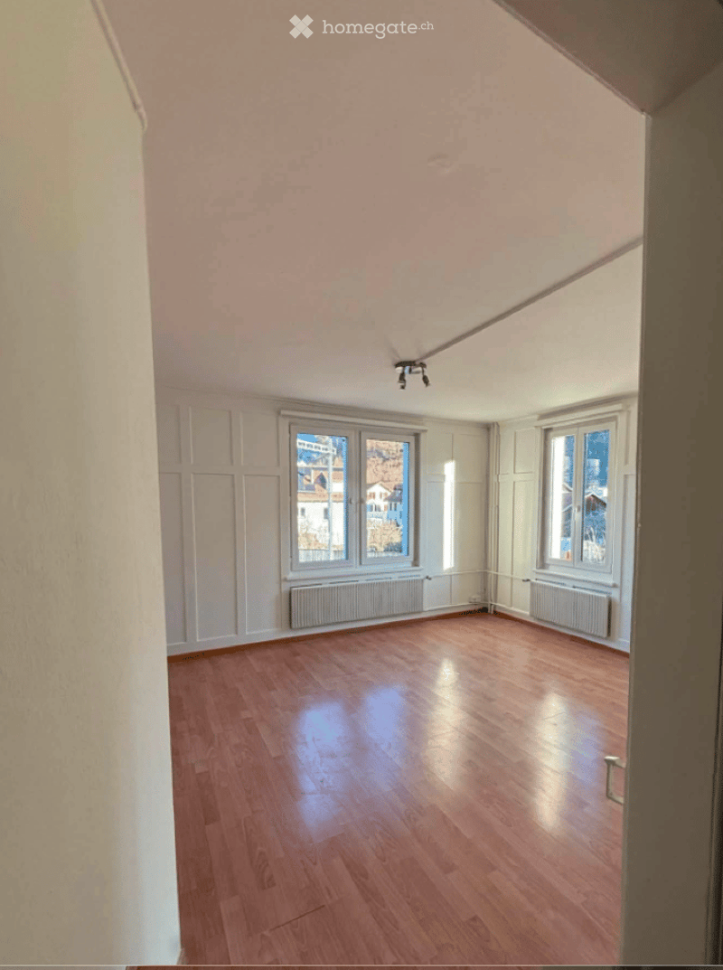 Empty room with wooden flooring, white walls, and large windows offering a view of the outside. No furniture or equipment is present.