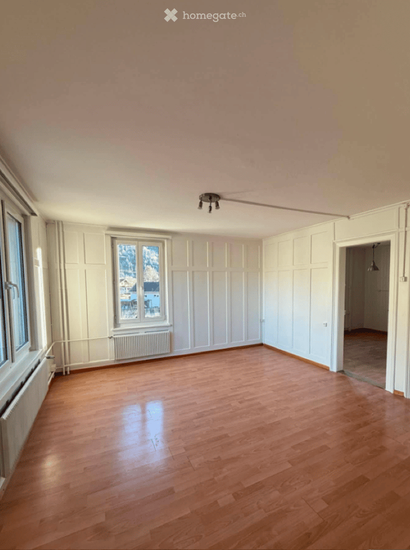 Empty room with wooden flooring, white walls, and large windows offering a view of the outside. No furniture or equipment is present.