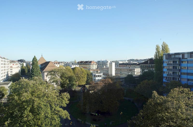 Aerial view of a park area surrounded by residential buildings, featuring trees, pathways, and benches.