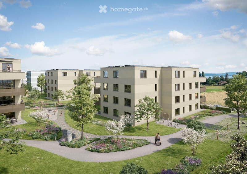 A modern residential complex with multiple apartment buildings, surrounded by landscaped gardens, pathways, and outdoor seating areas.