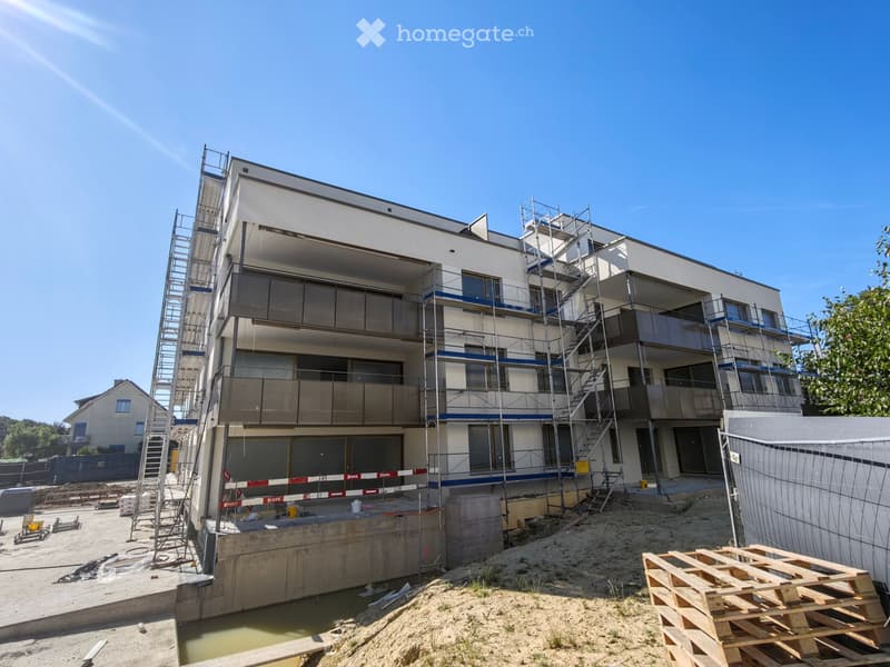 Modern multi-story residential building under construction with scaffolding, balconies, and a raised ground floor.