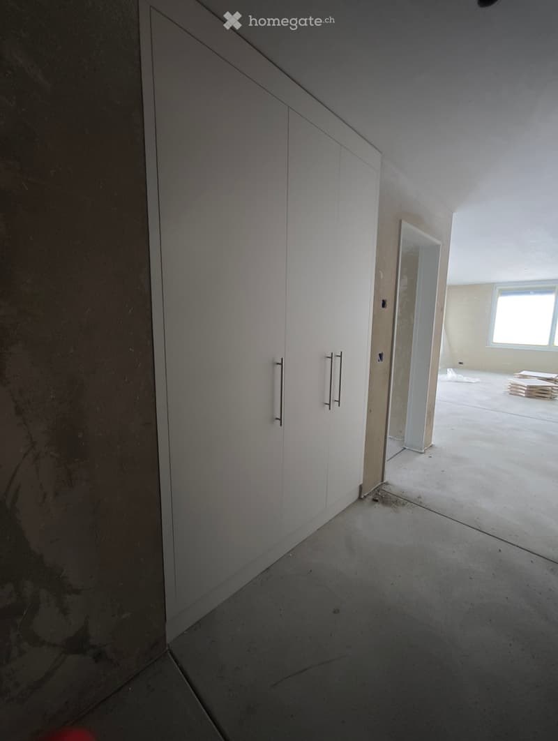 Empty room with white built-in closet, concrete floor, and a doorway leading to another room with a window.