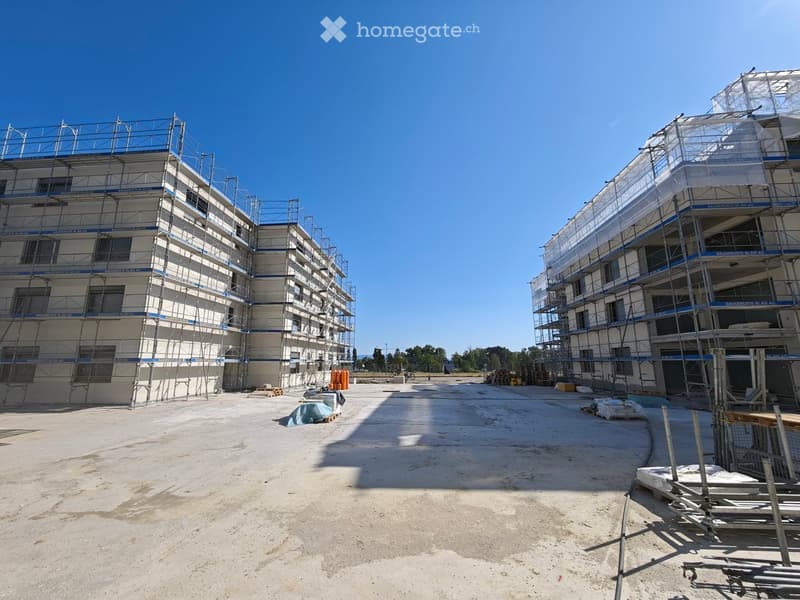 Two multi-story buildings under construction with scaffolding, surrounded by construction materials and equipment.