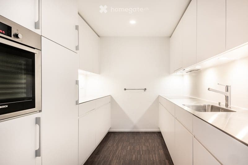 Modern, minimalist kitchen with white cabinets, dark wood flooring, stainless steel oven, and sink.