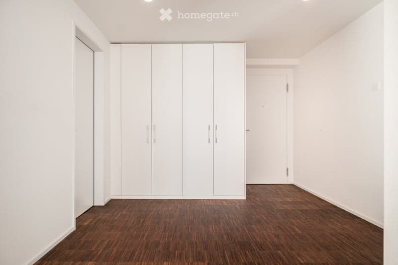 Empty room with white walls, wooden flooring, and built-in white wardrobes. No furniture or personal items present.