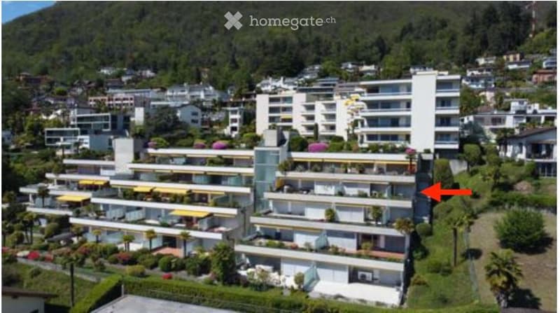 Aerial view of a multi-story residential complex with numerous balconies and terraces, surrounded by greenery and neighboring buildings.
