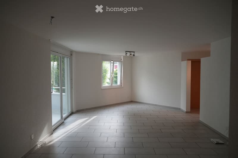 Empty room with tiled floor, white walls, large window, and sliding glass door leading to a balcony.