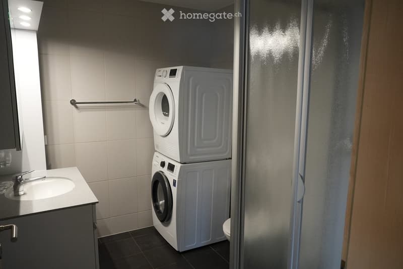 Modern bathroom with a sink, mirror, towel rack, and stacked washing machine and dryer unit.