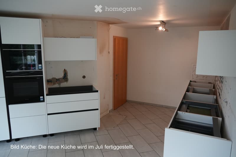 Modern kitchen with white cabinets, an oven, and tiled flooring. The cabinets are partially assembled, and the walls show some unfinished areas.