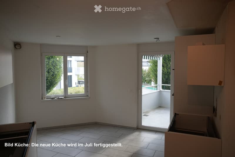 Empty room with tiled floor, white walls, and two large windows. One window opens to a balcony area with outdoor furniture visible.