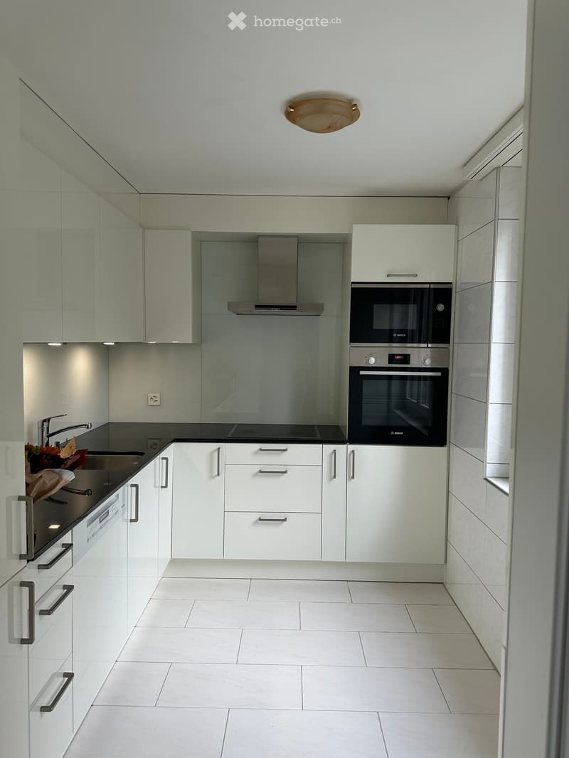 Modern kitchen with white cabinets, stainless steel appliances, and a black countertop. Features include a sink with a faucet, an oven, a microwave, and a decorative flower arrangement on the counter.