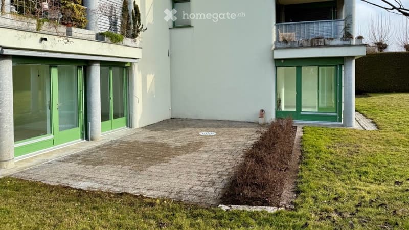Two-story building, white walls, green doors, brick paved area, terrace, bush in front
