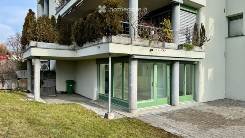 white apartment building, 2nd floor balcony, green windows, trash bin