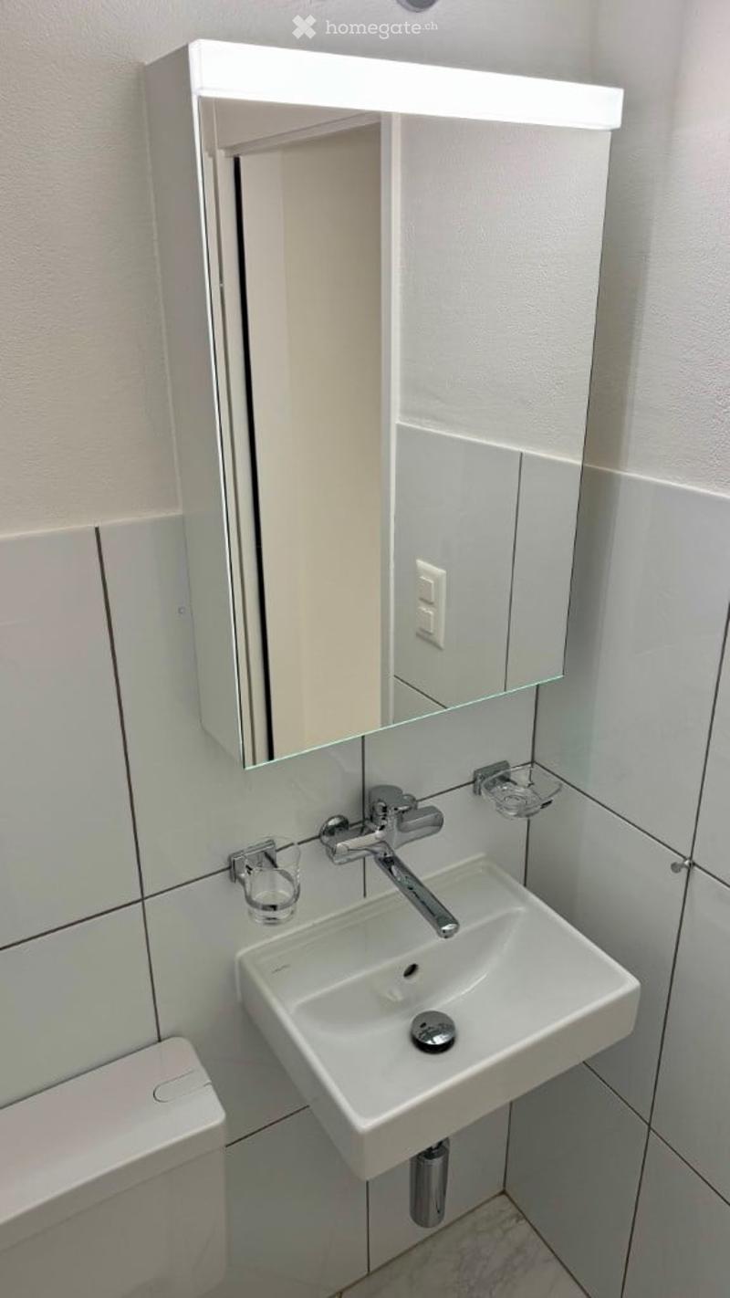 Small white bathroom with mirror cabinet, white toilet, white sink, and chrome faucet