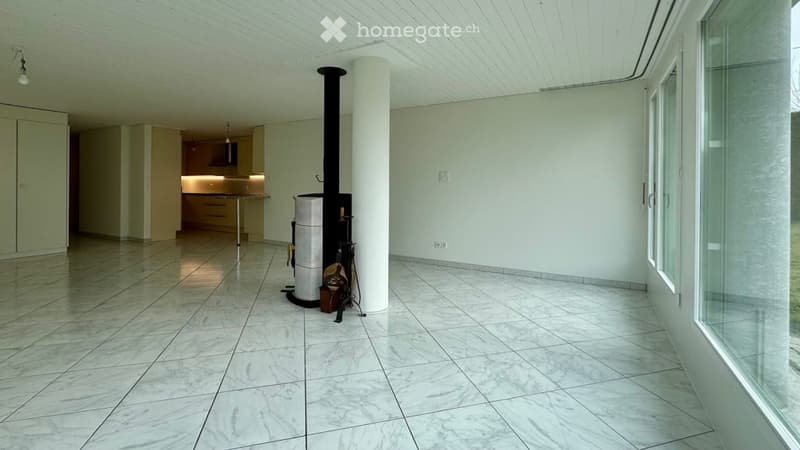 Bright, open room with a modern fireplace, white tiled floor, and a small kitchen area with cabinets and a table.