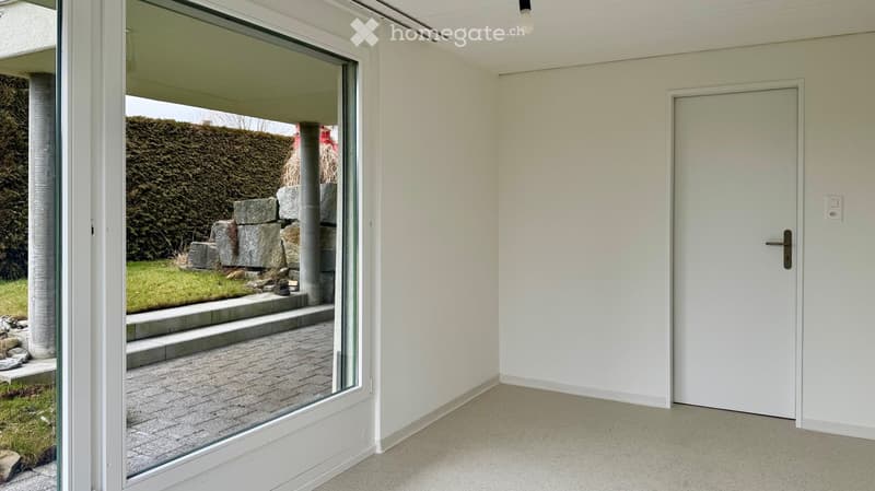 Room with sliding glass door to patio, white walls and floor, light switch