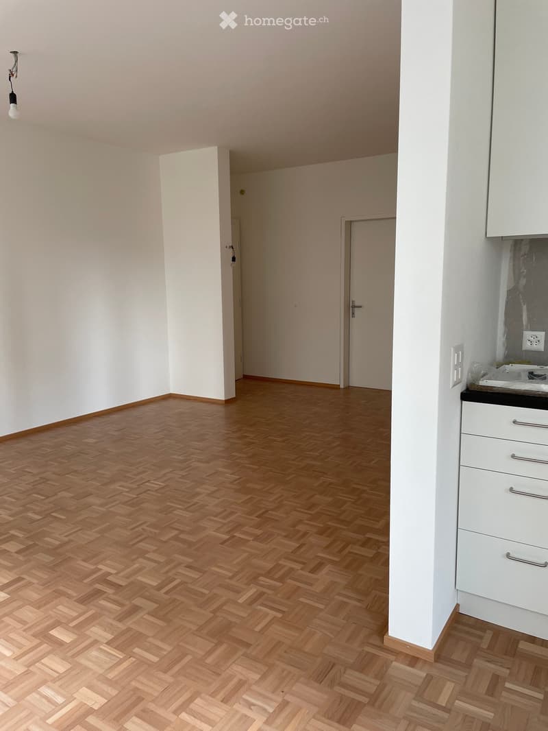 Empty room with wooden herringbone flooring, white walls, and a small white cabinet with drawers on the right side.