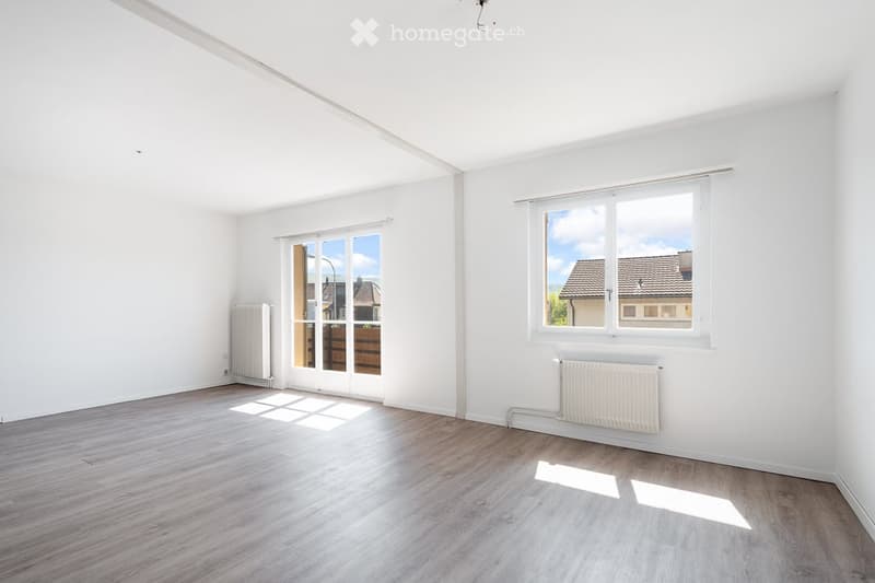 Empty room with white walls, light wooden flooring, large windows, and a sliding glass door leading to an outdoor area.