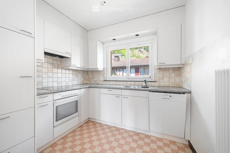 Modern kitchen with white cabinets, granite countertops, and a window overlooking a garden. Features an oven, dishwasher, and sink.