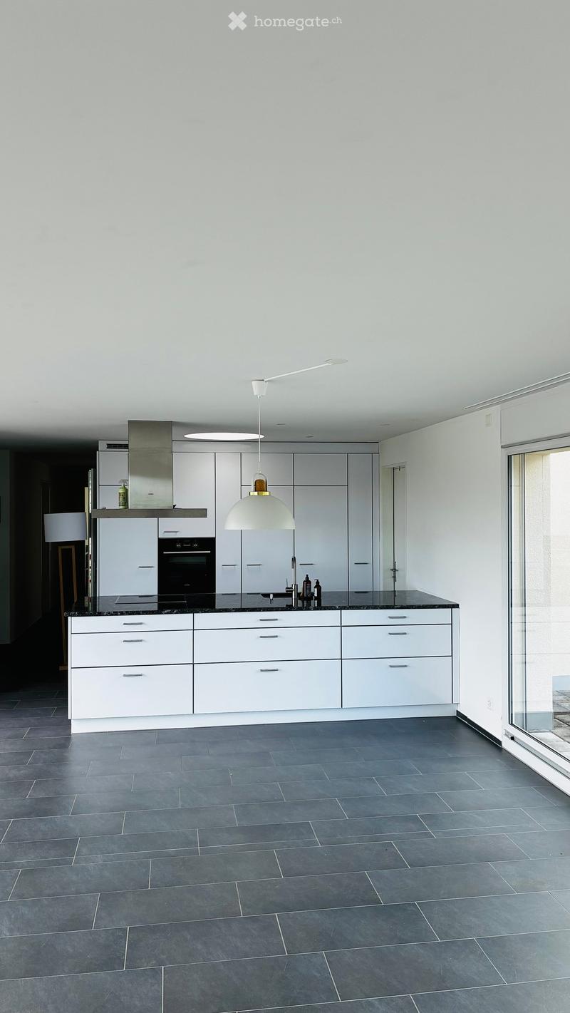 Modern kitchen with white cabinets, dark countertops, and a central island. Features a pendant light, built-in oven, and a sleek faucet.