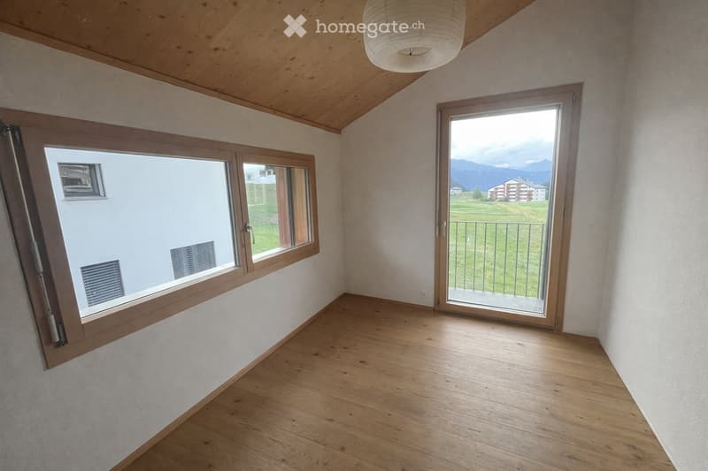 Empty room with wooden flooring, large windows, and a sliding door leading to a balcony with a scenic mountain view.