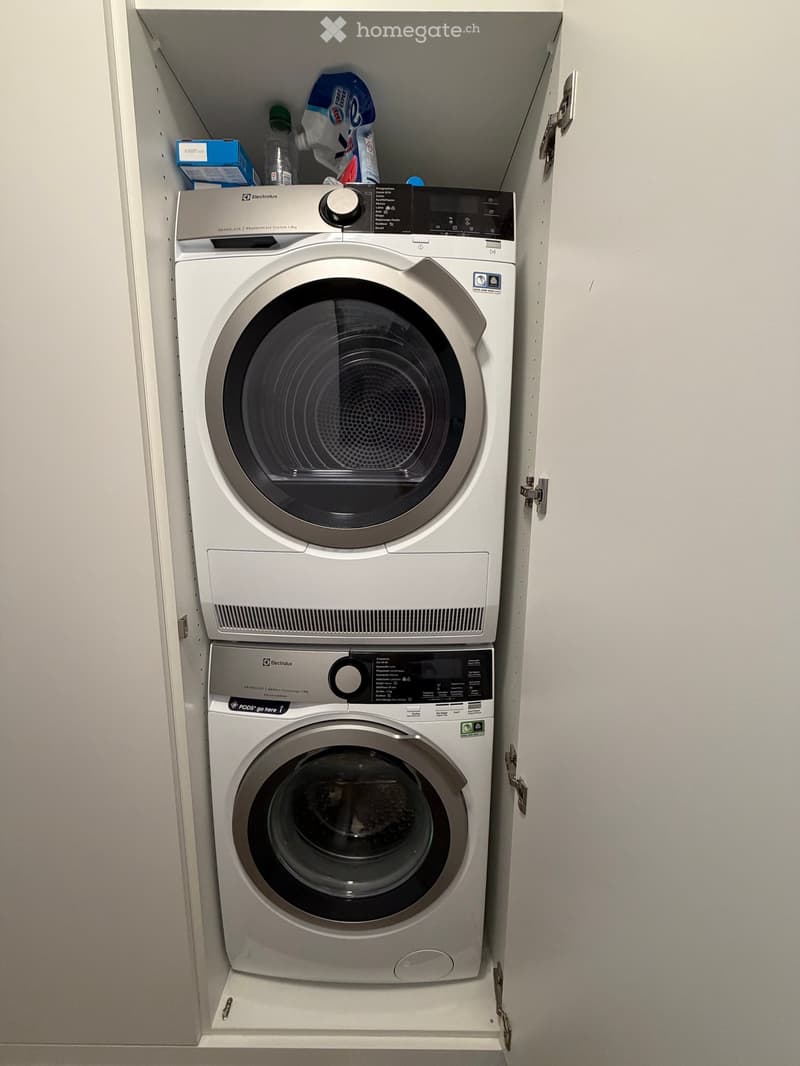 A compact, modern bathroom with a stacked washing machine and dryer unit, featuring a sleek design and control panel.