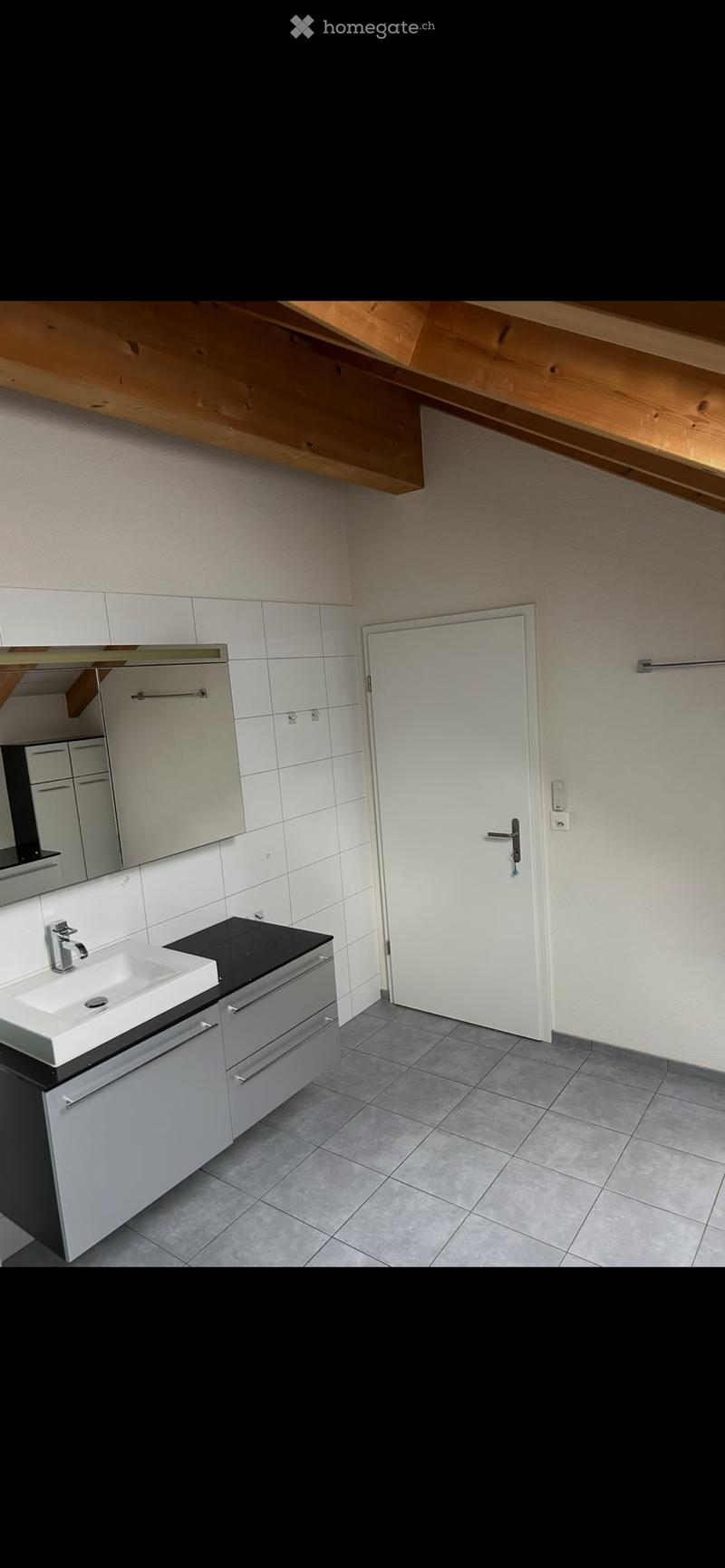 Modern bathroom with white tiles, a white sink, a mirror, and built-in cabinets. The room features a grey tiled floor and a white door.