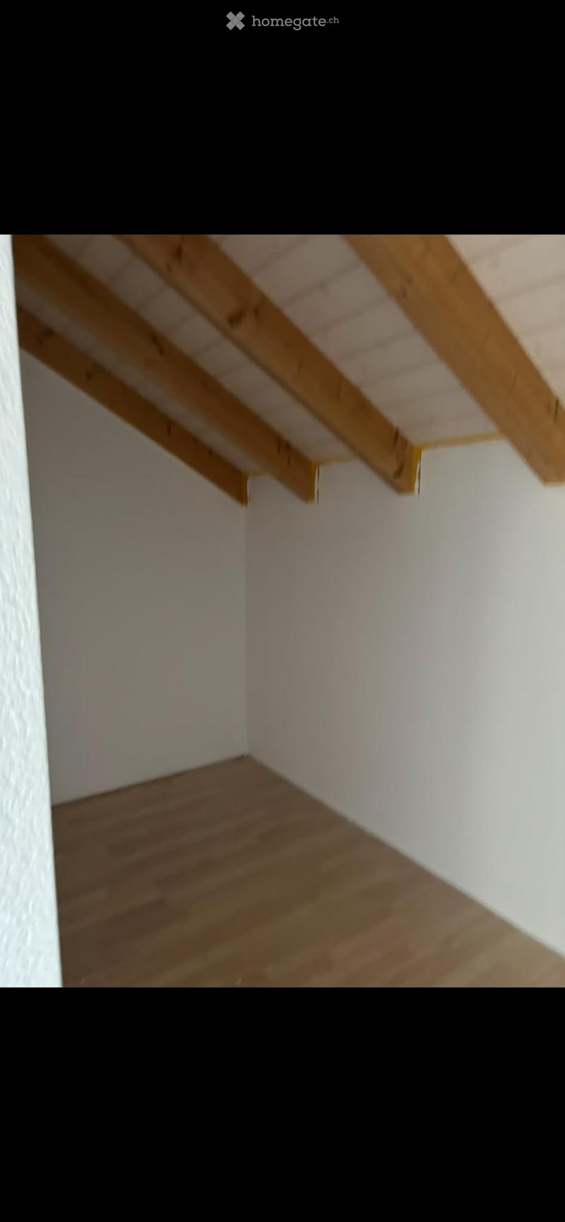 Empty attic space with wooden beams and light-colored wooden flooring, white walls, and exposed wooden ceiling beams.