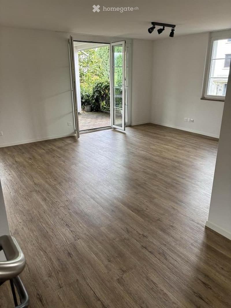 Empty room with wooden flooring, large sliding glass doors leading to a balcony, and a window on the opposite wall.