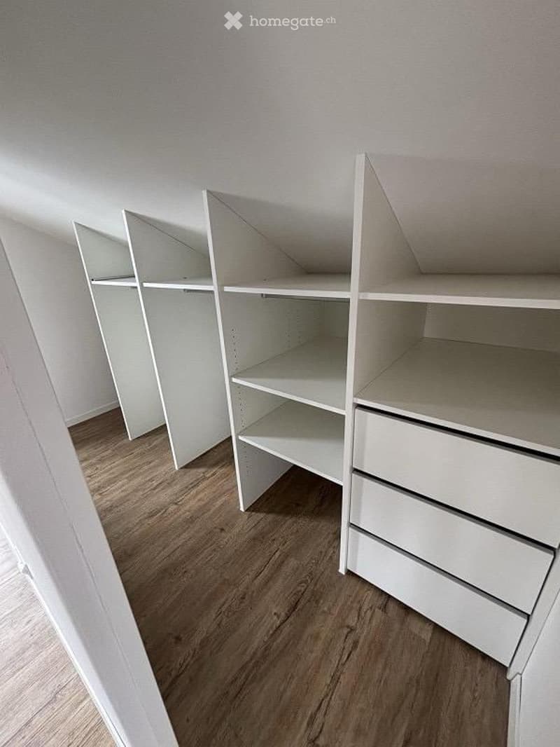 Empty closet with white built-in shelving units and drawers, wooden flooring, and white walls.