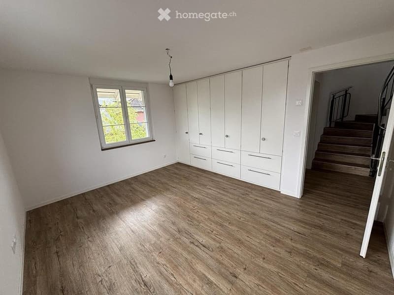 Empty room with white walls, wooden flooring, built-in white cabinetry, and a window with a view of greenery.