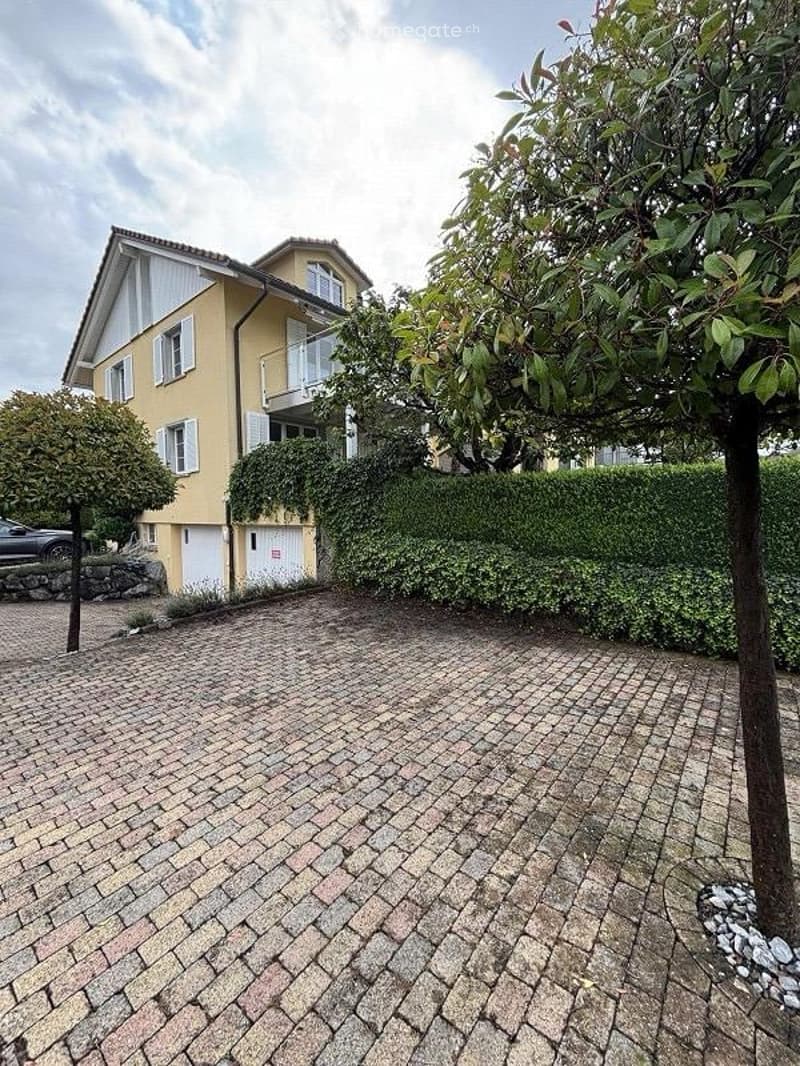 Two-story yellow house with white trim, balcony, garage, and parking area.