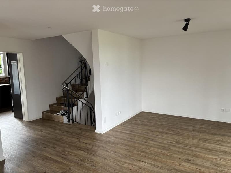 Empty room with wooden flooring, white walls, and a staircase leading upwards. No furniture or equipment present.