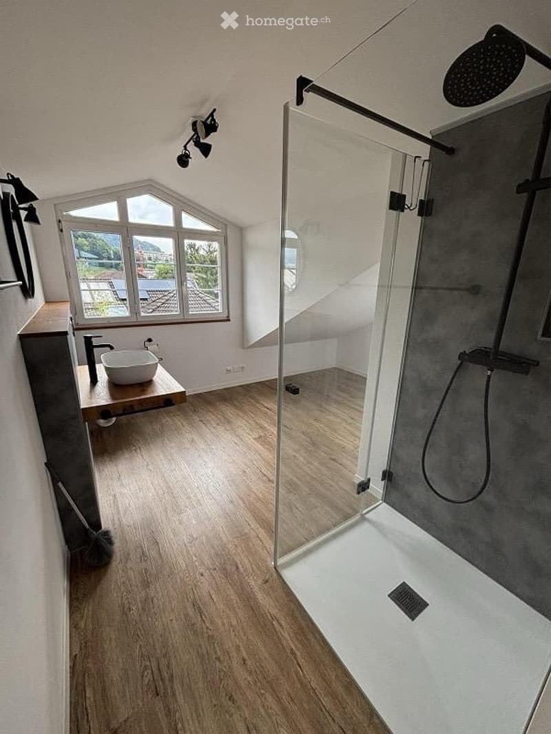 Modern bathroom with wooden flooring, a glass-enclosed shower, a sink on a wooden vanity, and a skylight window offering a view.