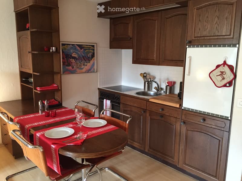 kitchen with dining area, wooden floor, table with 4 chairs, wooden shelves, wooden cupboards, black oven, sink, refrigerator, kitchen utensils, wine glasses, plates