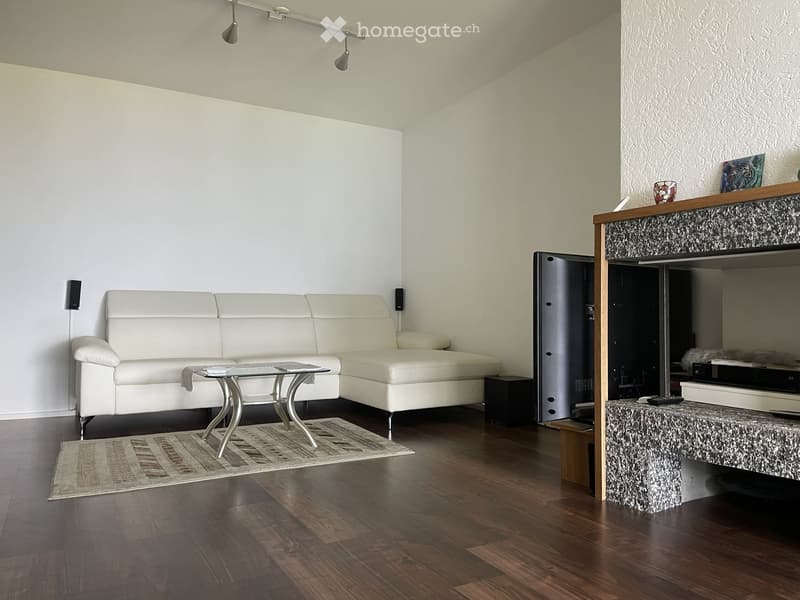 Modern living room with white leather sofa, glass coffee table, wooden floor, fireplace, and speakers.