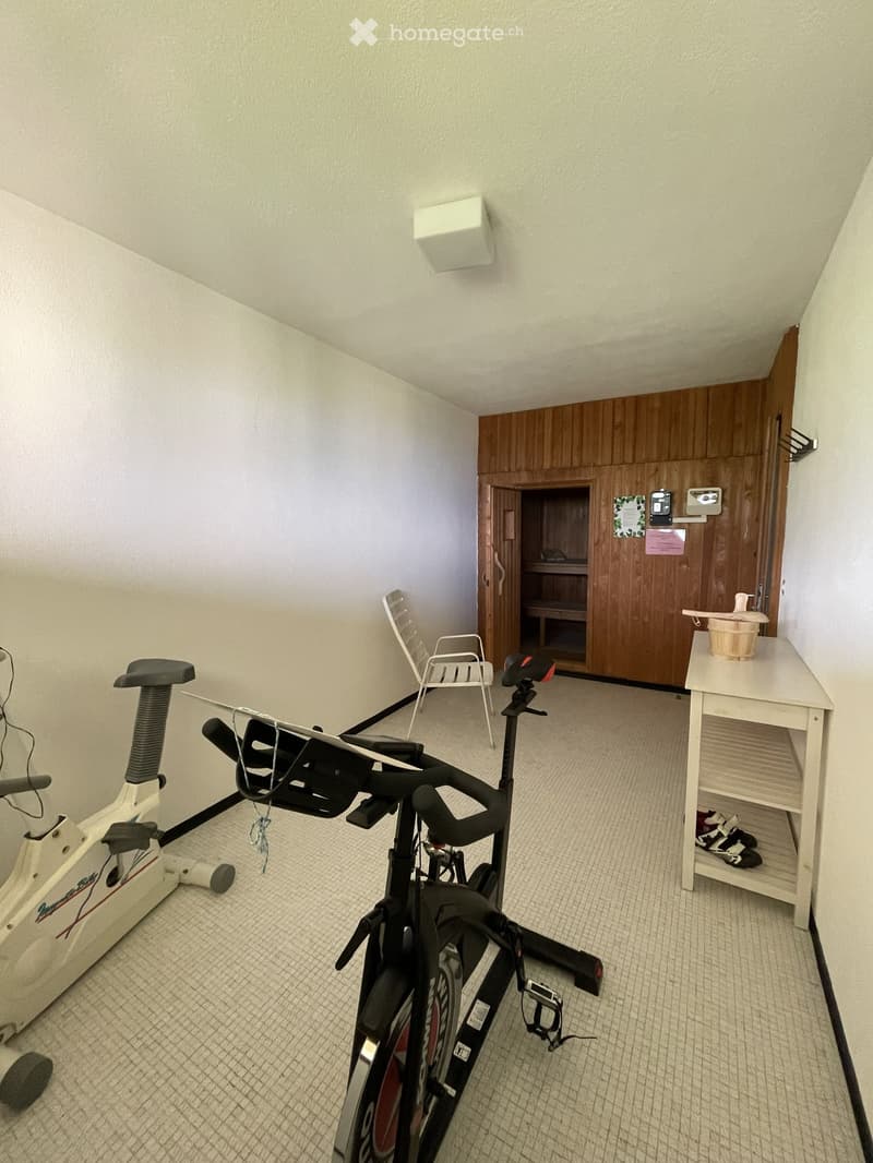 Exercise room with a stationary bike, exercise bike, two chairs, a small table with a basket, and a shelf with shoes.