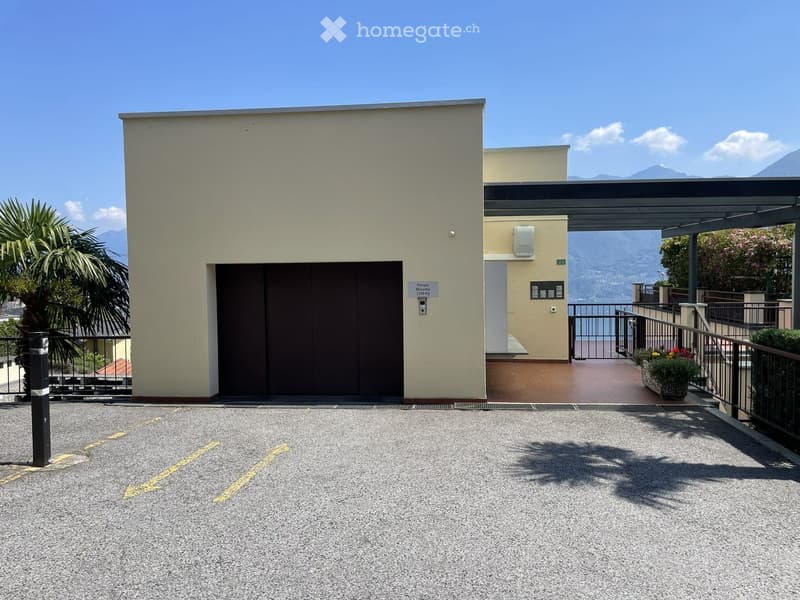 Modern building entrance with a covered walkway, parking area, and scenic mountain view in the background.