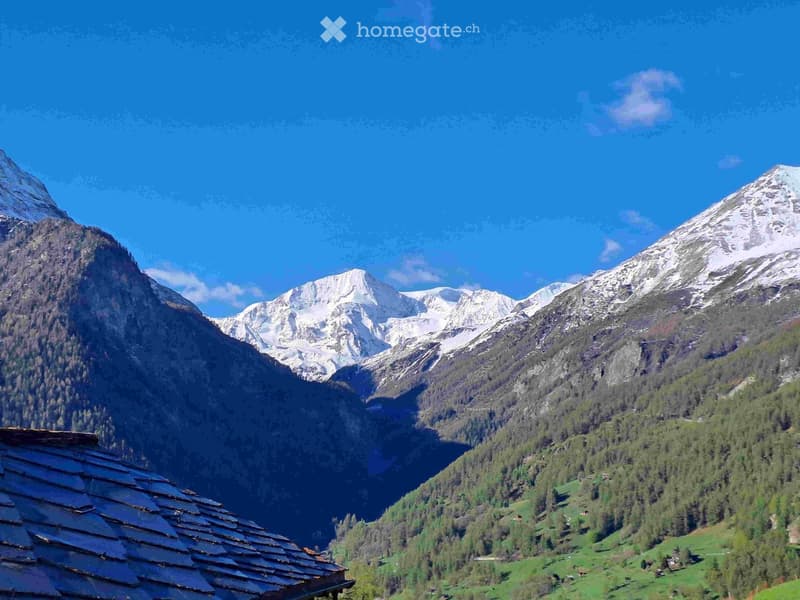 A scenic mountain landscape with snow-capped peaks, lush green valleys, and a traditional wooden roof visible in the foreground.