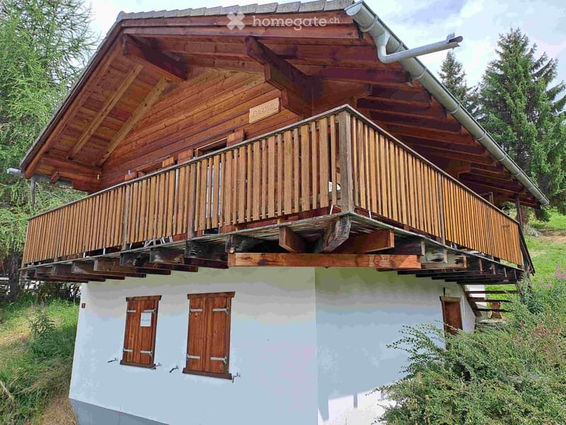 Two-story wooden house with a large balcony, white lower facade, and wooden upper facade. The balcony has wooden railings and a sign reading "EVELYN'S" above it.