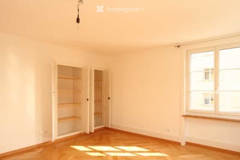 Empty room with wooden flooring, white walls, a built-in closet, and a large window letting in natural light.