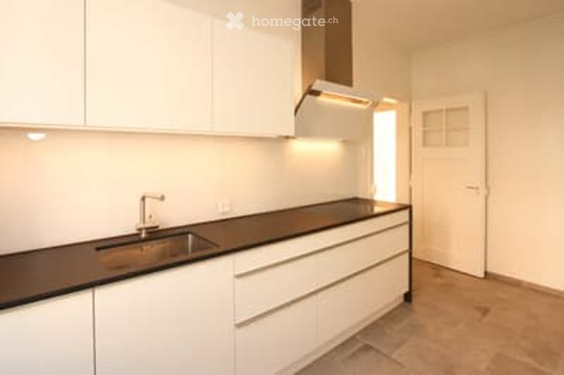 Modern kitchen with white cabinets, black countertop, stainless steel sink, and a built-in range hood.