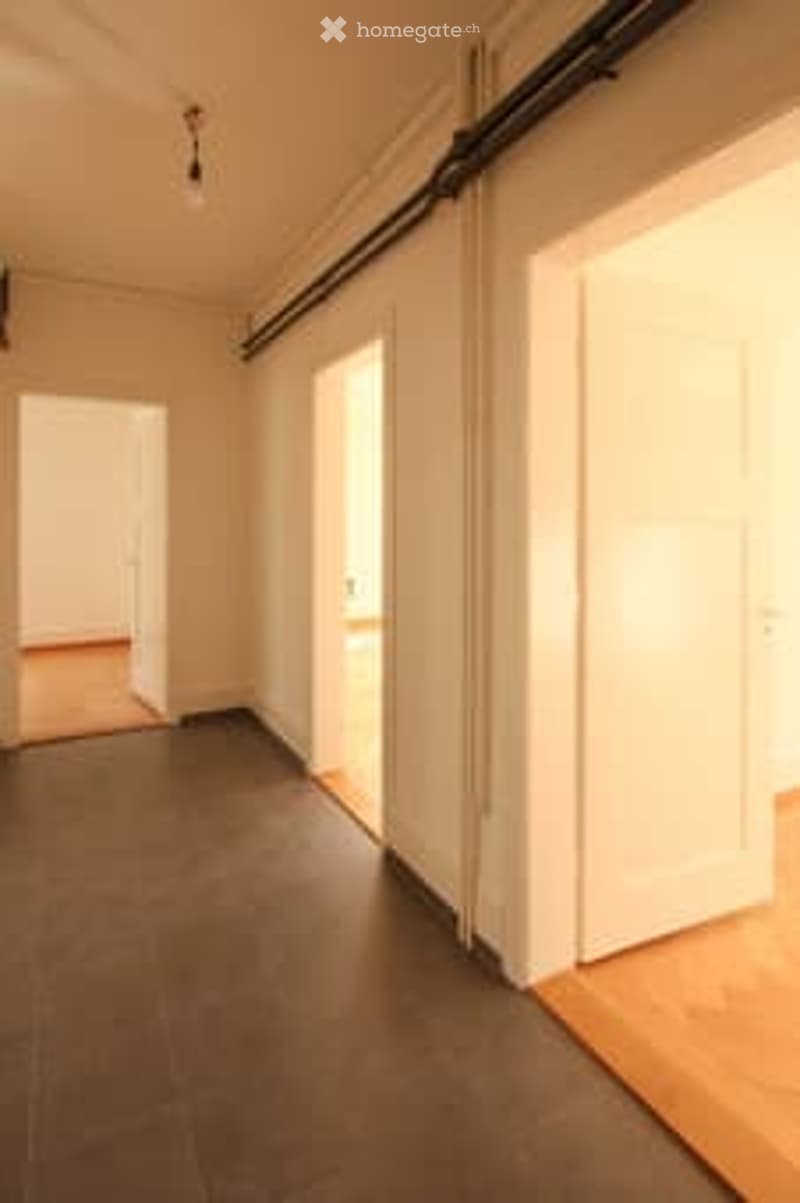 Empty room with dark grey tiled floor, white walls, and large white sliding doors leading to another space.