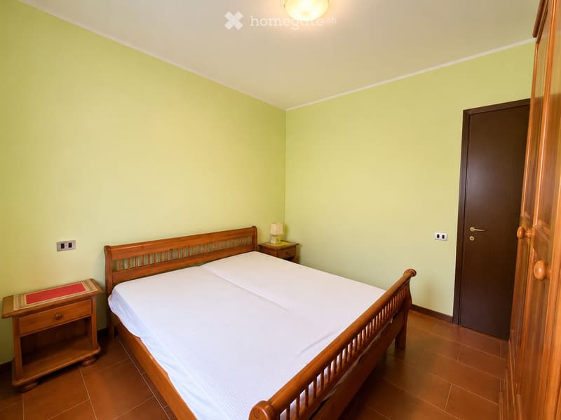 Cozy bedroom with a wooden bed, white bedding, a nightstand with a lamp, and a wooden drawer unit.