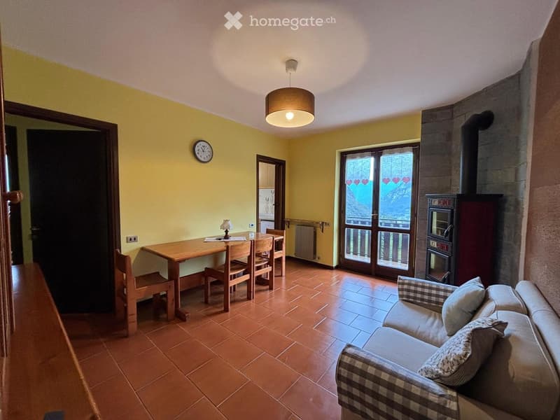 Bright living room with yellow walls, terracotta tiled floor, a sofa, a wooden dining table with chairs, a wall-mounted clock, and a hanging lamp.