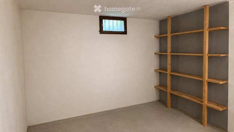 Empty room with white walls, wooden shelving unit, and a small window with a brown frame.