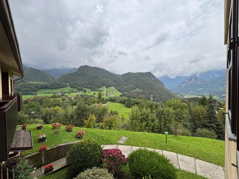 Balcony overlooking a lush green valley with rolling hills and distant mountains under a cloudy sky.