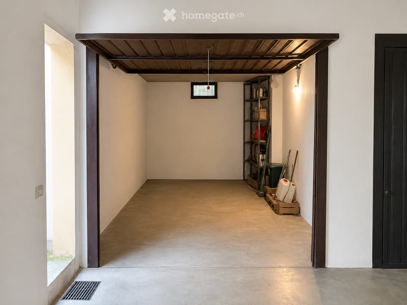 Empty garage with concrete floor, white walls, and a metal shelving unit holding various items. The space features a large open doorway and a small window.
