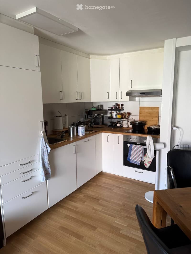 Modern kitchen with white cabinets, wooden countertops, and a wooden floor. Features an oven, fan, sink, and various kitchen appliances and utensils.
